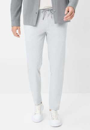 Pantalons de jogging gris clair avec une texture lisse et une taille élastique, dotés d'un cordon de serrage et d'une coupe ajustée, associés à des baskets blanches.
