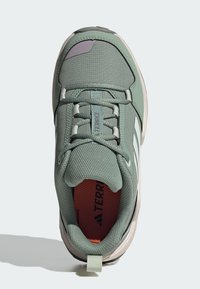 Grønn tekstil sneaker med teksturert overflate, forsterkede snørehull, kontrasterende lilla detaljer og en trekkstropp bak.