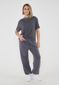 T-shirt grigio a maniche corte abbinato a pantaloni larghi grigi. Tessuto morbido con vestibilità rilassata; indossato con sneakers bianche da ginnastica. Design semplice.