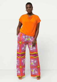 Heldere oranje gedrapeerde top gecombineerd met wijde broek met een levendig bloempatroon in roze, geel en rood. Glad textiel.