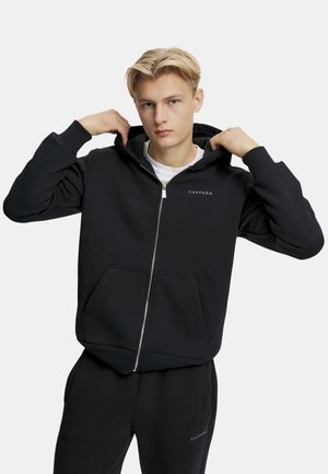 Sort zip-up hoodie lavet af bomuldsblanding, med en justerbar hætte, frontlommer og et logo på brystet. Styliseret med matchende bukser.