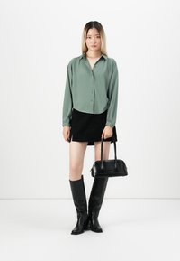 Green button-up shirt with long sleeves, black suede skirt, knee-high black leather boots, and a small black handbag.