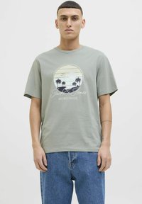 Camiseta de algodón de color verde claro con un gráfico circular de playa que incluye palmeras, el nombre de la marca "Jack & Jones" y un corte relajado.