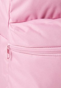 Roze stoffen rugzak van textuurmateriaal, met een ritsvak en stiksels, waarmee een strakke uitstraling wordt benadrukt.