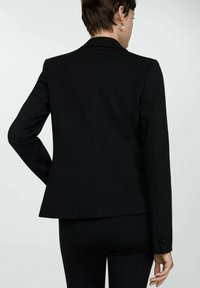 Black tailored blazer with long sleeves, notch collar, fitted back, and subtle seam details. Made from structured fabric.