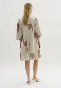 Knee-length beige klänning med stora abstrakta bruna mönster, puffiga ärmar och avslappnad passform. Slätt tyg med en lätt lyster.