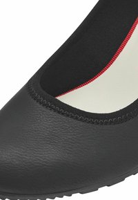 Scarpa piatta sintetica nera con punta arrotondata, tomaia texturizzata, fodera rossa a contrasto e rifinitura elastica nera attorno all'apertura.