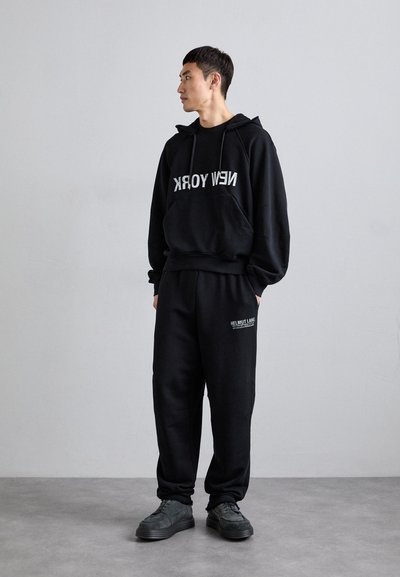 Czarna bluza z kapturem z napisem "NEW YORK" oraz dopasowane czarne spodnie dresowe z logo "HELMUT LANG", noszone z szarymi butami. Miękka tkanina, luźny krój.