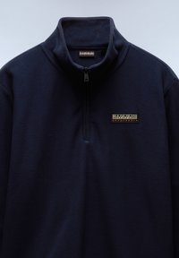 Sudadera de forro polar azul marino con un cuello alto, media cremallera y parche de logo bordado en el pecho. Textura suave con un acabado liso.
