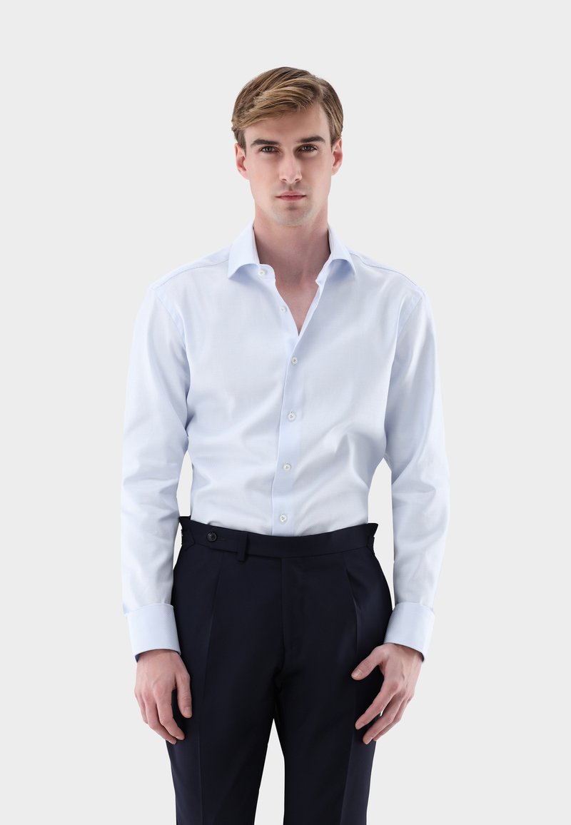 Hellblaues Hemd aus glattem Stoff mit spitzem Kragen, durchgehendem Knopfverschluss und langen Ärmeln mit kontrastierenden Manschetten, kombiniert mit dunkler Hose.