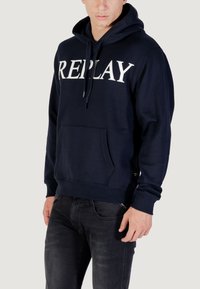Felpa blu navy realizzata in cotone con tasca frontale, caratterizzata da un grande logo bianco "REPLAY" sul petto. Cappuccio con cordino e polsini a costine.