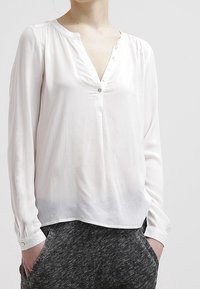 Vit blus med lång ärm, V-ringning och sju knappar fram. Mjuk, lättvikts tyg med en något genomskinlig textur och avslappnad passform.