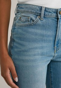 Helleblaue Jeans aus Denim mit einer körpernahen Passform, klassischem Five-Pocket-Stil, gesteppten Akzenten und einem Knopfverschluss.