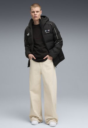 Zwarte pufferjack met witte accenten en BMW-logo, zwarte crewneck, brede beige broek, witte sneakers; simpel, modern ontwerp.