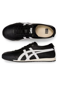 Mustat nahkakengät urheiluun, joissa on valkoiset sivuraidat, tekstuurinen kumipohja ja kontrastivärinen ommel; varustettu nauhoituksella ja pehmustetulla kauluksella.