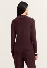 Bordeaux rotes Langarmoberteil mit lockerer Passform, weicher Textur und umgeschlagenem Kragen, ausgestattet mit einem sauberen Saum und hochgestellten Ärmeln.