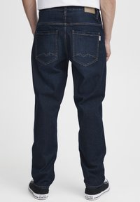 Jeans de mezclilla azul oscuro con corte recto, que presentan costuras amarillas en contraste y dos bolsillos traseros con solapas en ángulo.