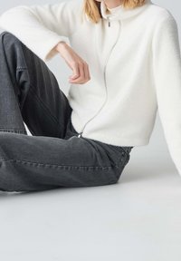 Hvid fleece zip-up sweater med høj krave, parret med mørkegrå denim jeans. Sweateren har en glat tekstur og en afslappet pasform.