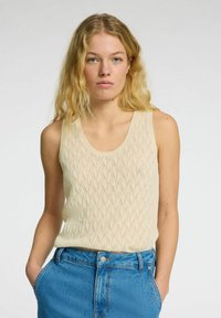 Beige, strikket tanktop med bølget mønster. Har en rund halsudskæring og brede stropper. Kombineret med højtaljede blå denimshorts.