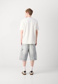 T-shirt bianco a maniche corte e pantaloni cargo in denim blu chiaro con due tasche laterali. Indossato con calzini bianchi e sandali marroni.