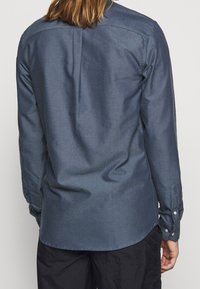 Donkerblauw shirt met lange mouwen gemaakt van een gestructureerde stof, voorzien van een rugpas en een afgeronde zoom, met manchetten sluitbaar met knopen en een casual pasvorm.