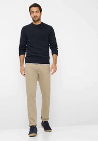 Marineblauer Strickpullover mit geripptem Muster, khakifarbene Slim-Fit-Hose und dunkelblaue Sneaker mit braunen Sohlen. Klare, schlichte Gestaltung in neutraler Umgebung.