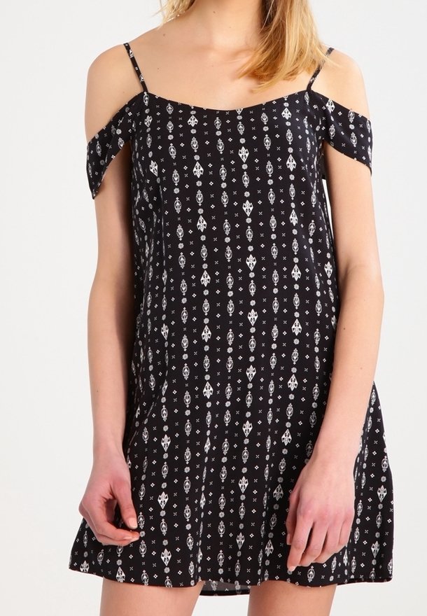 Vestido negro con diseño de hombros al descubierto, adornado con patrones geométricos blancos. Hecho de un tejido ligero, cuenta con tirantes delgados y una falda acampanada.