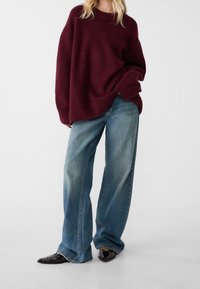 Pull en tricot surdimensionné couleur bordeaux avec un col rond, associé à un jean taille haute bleu clair à jambes larges et des ballerines noires pointues.