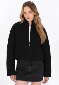 Sort quiltet cropped jakke med høj krave, frontlynlås og to påsyede lommer. Kombineret med et sort denimskørt.