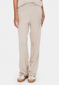 Helle beige Strick-Sweatpants mit elastischem Bund, geradem Bein-Design und weicher Textur, kombiniert mit lässigen mehrfarbigen Sneakers.