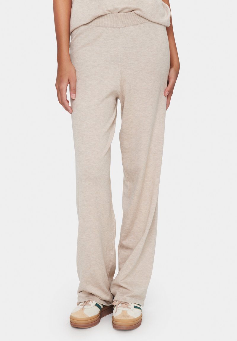 Helle beige Strick-Sweatpants mit elastischem Bund, geradem Bein-Design und weicher Textur, kombiniert mit lässigen mehrfarbigen Sneakers.