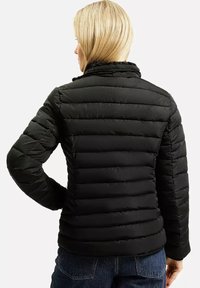 Nadmuchana czarna kurtka z poziomymi przeszyciami, wysokim kołnierzem i gładką teksturą. Posiada dopasowany krój i noszona jest na niebieskich dżinsach.