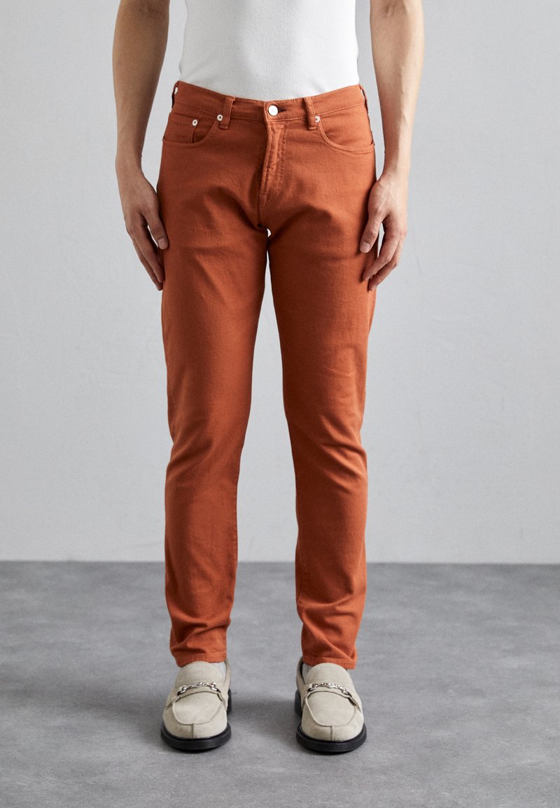 Orange, slim-fit byxor i bomull. Har bakfickor och dragkedja med knappstängning. Bärs med ljusa loafers.