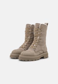 Beige veterschoenen met een militaire uitstraling, gemaakt van zacht suede, met ribbelige rubberen neuskap en textuurzolen, voorzien van een verstevigde hak en stikdetails.