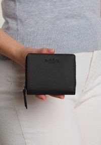 Black leather wallet with a smooth texture, rectangular shape, zip closure, and logo embossed on the front. Accented with a zipper pull.