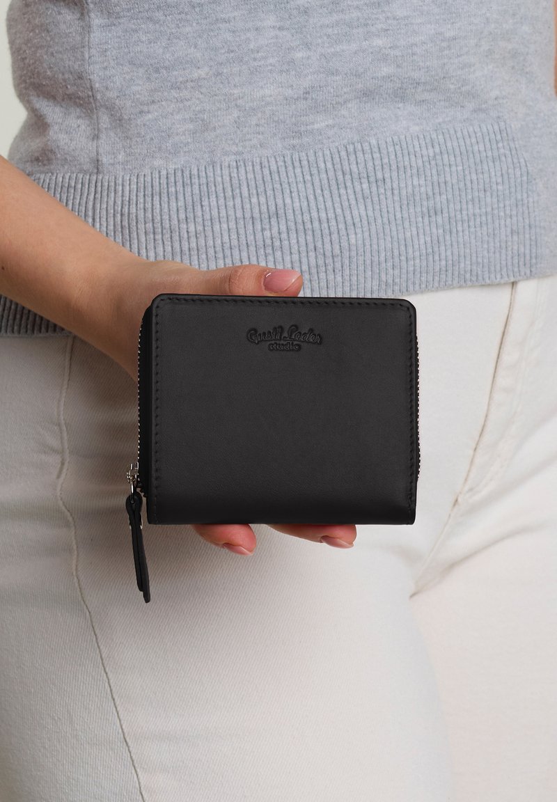 Black leather wallet with a smooth texture, rectangular shape, zip closure, and logo embossed on the front. Accented with a zipper pull.
