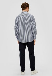 Gestreept blauw-wit langemouwen shirt met een button-down kraag, gecombineerd met donkere broek en witte sneakers. Zichtbare stikseldetails.