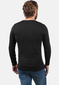 Langærmet sort skjorte lavet af bomuld, med en tætsiddende design og glat tekstur, parret med blå jeans og en simpel rygudskæring.