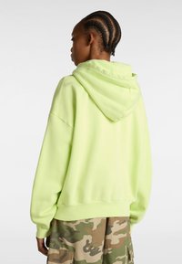 Neon green hoodie with a soft texture, oversized fit, and a drawstring hood, paired with camouflage cargo pants.