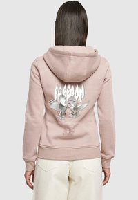 Růžová mikina s kapucí, předními kapsami a grafikou dvou létajících holubic s nápisem "SVOBODA" nad nimi. Měkká textura, volný střih.