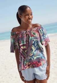 Off-shoulder top met kleurrijke abstracte patronen in paars, groen en rood; heeft een geraffineerde halslijn en korte mouwen. Gecombineerd met lichtblauwe shorts.