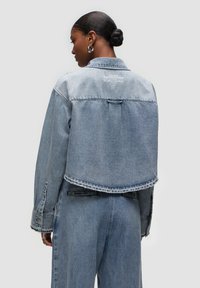 Giacca in denim blu con design corto, orlo grezzo e dettagli ricamati sul retro. Presenta un colletto standard e polsini con bottoni.