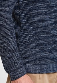 Mörkblå stickad tröja med ett texturerat mönster, med ribbat nederkant och ärmar. Tillverkad av mjukt material, har den en avslappnad passform.