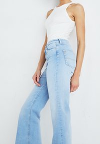 Ljusblå högmidjade jeans med utsvängd ben, femficksdesign och ljusa sömnadsdetaljer; tillverkade av denimtyg.