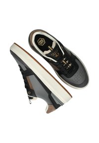 Zwarte en grijze sneakers met een gestructureerd oppervlak, voorzien van een witte zool, bruine accenten en gouden details op de tong en zijkanten.