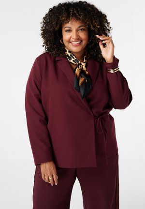 Bordeaux blazer met een strik in de taille, lange mouwen en een diepe V-hals, gecombineerd met een gemêleerde sjaal in zwart en goudtinten.