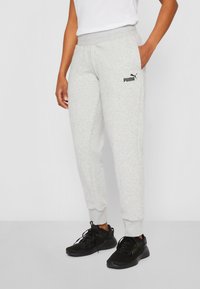 Lysegrå sweatpants med ribbede manchetter, elastisk talje og sort Puma-logo på venstre lår, parret med sorte sportssko.