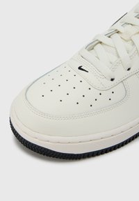 Λευκό δερμάτινο παπούτσι σνίκερ με διάτρητο μπροστινό μέρος, σχεδίαση με κορδόνια και μαύρη λαστιχένια σόλα. Διαθέτει μικρό μαύρο λογότυπο κοντά στα κορδόνια.