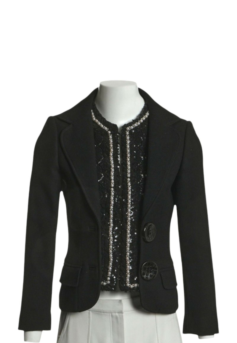 Blazer noir ajusté avec deux gros boutons, porté sur un top noir à sequins avec un bord en perles, associé à un pantalon plissé clair.