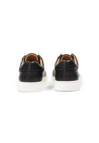 Zapatillas de cuero negro con una suela de goma blanca, con un diseño redondeado, costuras en contraste y una textura suave. Vista trasera mostrada.